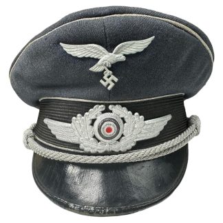 "High-resolution photograph featuring a German Luftwaffe officer's visor cap, meticulously crafted with a peaked crown, silver braided chinstrap, and distinctive Luftwaffe insignia, symbolizing authority and prestige within the German air force during World War II. This visor cap evokes the historical significance of aerial warfare, military leadership, and the distinctive attire of Luftwaffe officers during the wartime era."