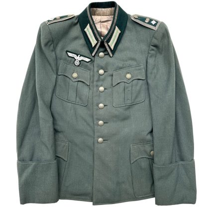 World War II German Infanterie-Regiment 69 NCO uniform jacket in field-grey wool, featuring silver-toned buttons, four front pockets with flaps, and green collar tabs with silver piping. The jacket includes an embroidered Wehrmacht eagle insignia on the right chest and shoulder boards with rank insignia. The dark green collar and cuffs, along with detailed trim, indicate the rank and unit affiliation of a non-commissioned officer.