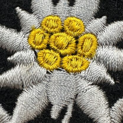 WWII German Waffen-SS Gebirgsjäger insignia featuring an embroidered Edelweiss flower with white petals, a yellow center, and a black oval background, symbolizing mountain troops.