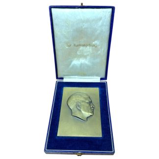 Metal plaque featuring the side profile of Adolf Hitler in relief, presented in a blue velvet box with white interior lining. The text 'Zur Namensgebung' is visible on the inside of the lid. Historical object from the period of the Third Reich.