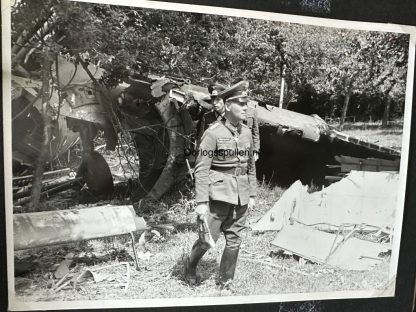 Black-and-white photograph of Field Marshal Erwin Rommel walking through a wooded area near the wreckage of a destroyed British glider during D-Day, wearing a military uniform with a peaked cap and boots. The scene depicts a moment of inspection or reconnaissance during World War II.