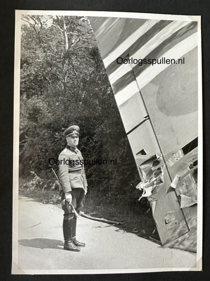 Black-and-white photograph of Field Marshal Erwin Rommel walking through a wooded area near the wreckage of a destroyed British glider during D-Day, wearing a military uniform with a peaked cap and boots. The scene depicts a moment of inspection or reconnaissance during World War II.