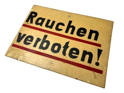 Metal German sign with the text 'Rauchen verboten!' from World War II, featuring a yellow background, black text with red underlining, and visible aging such as crackling and paint wear.