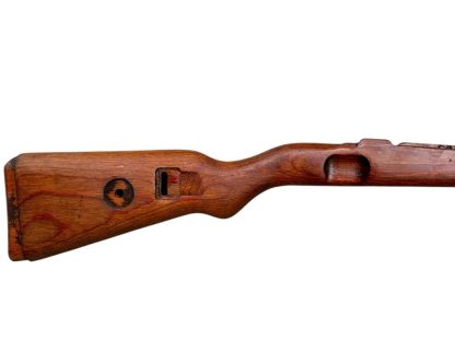 A vintage wooden rifle stock for a German WWII Mauser K98, showcasing a polished reddish-brown finish with visible wood grain texture. The design features a curved grip and cutouts for mounting hardware. The stock appears well-preserved with signs of age and use, such as minor scuffs and wear, adding to its historical authenticity.