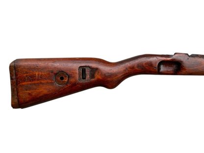 German WWII Mauser K98 wooden rifle stock, showcasing a rich reddish-brown finish, with visible wear and patina from age and use. The stock includes a cutout for the bolt handle and features slots for a sling, along with a detailed grain pattern typical of wartime production.