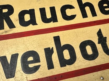 Metal German sign with the text 'Rauchen verboten!' from World War II, featuring a yellow background, black text with red underlining, and visible aging such as crackling and paint wear.