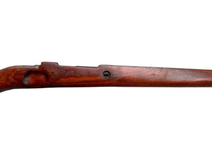 A vintage wooden rifle stock for a German WWII Mauser K98, showcasing a polished reddish-brown finish with visible wood grain texture. The design features a curved grip and cutouts for mounting hardware. The stock appears well-preserved with signs of age and use, such as minor scuffs and wear, adding to its historical authenticity.