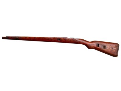 A vintage wooden rifle stock for a German WWII Mauser K98, showcasing a polished reddish-brown finish with visible wood grain texture. The design features a curved grip and cutouts for mounting hardware. The stock appears well-preserved with signs of age and use, such as minor scuffs and wear, adding to its historical authenticity.