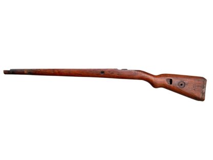 German WWII Mauser K98 wooden rifle stock, showcasing a rich reddish-brown finish, with visible wear and patina from age and use. The stock includes a cutout for the bolt handle and features slots for a sling, along with a detailed grain pattern typical of wartime production.