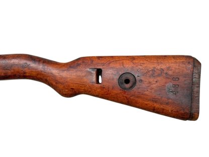 Image d'une crosse en bois allemande de fusil Mauser K98 de la Seconde Guerre mondiale, avec une finition brun foncé patinée et des découpes visibles pour fixer le mécanisme du fusil.