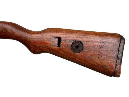 A vintage wooden rifle stock for a German WWII Mauser K98, showcasing a polished reddish-brown finish with visible wood grain texture. The design features a curved grip and cutouts for mounting hardware. The stock appears well-preserved with signs of age and use, such as minor scuffs and wear, adding to its historical authenticity.