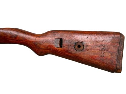 A vintage wooden rifle stock for a German WWII Mauser K98, showcasing a polished reddish-brown finish with visible wood grain texture. The design features a curved grip and cutouts for mounting hardware. The stock appears well-preserved with signs of age and use, such as minor scuffs and wear, adding to its historical authenticity.