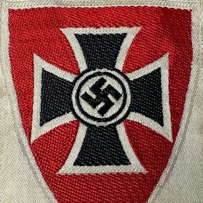 German Kyffhäuserbund emblem from World War II, featuring a black Iron Cross with a swastika in the center, set on a red shield with a cream-colored border, preserved in historical condition.