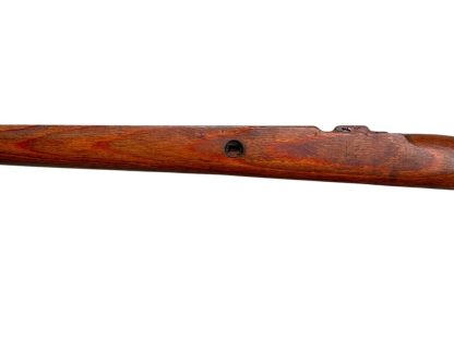 A vintage wooden rifle stock for a German WWII Mauser K98, showcasing a polished reddish-brown finish with visible wood grain texture. The design features a curved grip and cutouts for mounting hardware. The stock appears well-preserved with signs of age and use, such as minor scuffs and wear, adding to its historical authenticity.