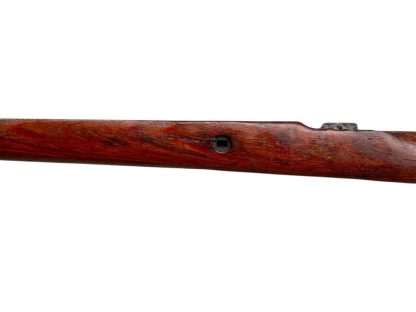 A vintage wooden rifle stock for a German WWII Mauser K98, showcasing a polished reddish-brown finish with visible wood grain texture. The design features a curved grip and cutouts for mounting hardware. The stock appears well-preserved with signs of age and use, such as minor scuffs and wear, adding to its historical authenticity.