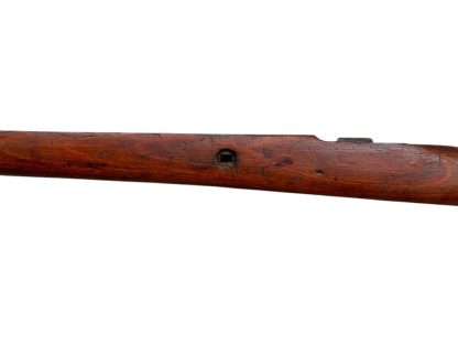 German WWII Mauser K98 wooden rifle stock, showcasing a rich reddish-brown finish, with visible wear and patina from age and use. The stock includes a cutout for the bolt handle and features slots for a sling, along with a detailed grain pattern typical of wartime production.