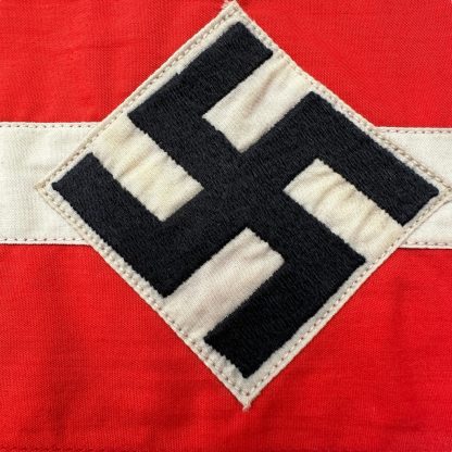 A historical Hitler Youth armband from World War II, made of red cotton with a white central section featuring a black swastika inside a circle.