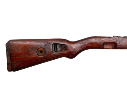 German WWII Mauser K98 wooden rifle stock, showcasing a rich reddish-brown finish, with visible wear and patina from age and use. The stock includes a cutout for the bolt handle and features slots for a sling, along with a detailed grain pattern typical of wartime production.