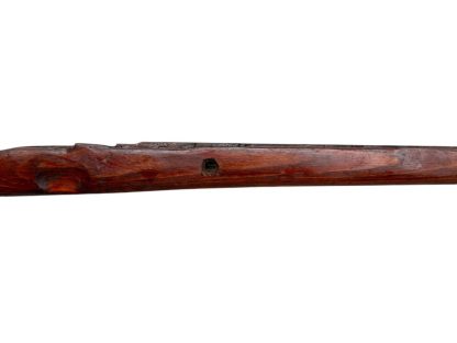 German WWII Mauser K98 wooden rifle stock, showcasing a rich reddish-brown finish, with visible wear and patina from age and use. The stock includes a cutout for the bolt handle and features slots for a sling, along with a detailed grain pattern typical of wartime production.