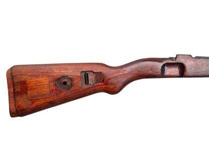 German WWII Mauser K98 wooden rifle stock, showcasing a rich reddish-brown wood finish with visible wear and aging, featuring the characteristic design for a bolt-action rifle. The stock includes a cutout for the bolt mechanism and a recess for the magazine well, highlighting its historical craftsmanship.