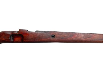 German WWII Mauser K98 wooden rifle stock, showcasing a rich reddish-brown wood finish with visible wear and aging, featuring the characteristic design for a bolt-action rifle. The stock includes a cutout for the bolt mechanism and a recess for the magazine well, highlighting its historical craftsmanship.