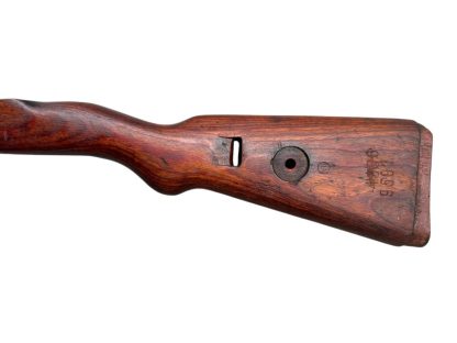 German WWII Mauser K98 wooden rifle stock, showcasing a rich reddish-brown wood finish with visible wear and aging, featuring the characteristic design for a bolt-action rifle. The stock includes a cutout for the bolt mechanism and a recess for the magazine well, highlighting its historical craftsmanship.