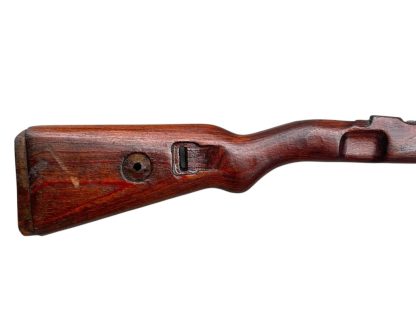 German WWII Mauser K98 wooden rifle stock, showcasing a rich reddish-brown wood finish with visible wear and aging, featuring the characteristic design for a bolt-action rifle. The stock includes a cutout for the bolt mechanism and a recess for the magazine well, highlighting its historical craftsmanship.