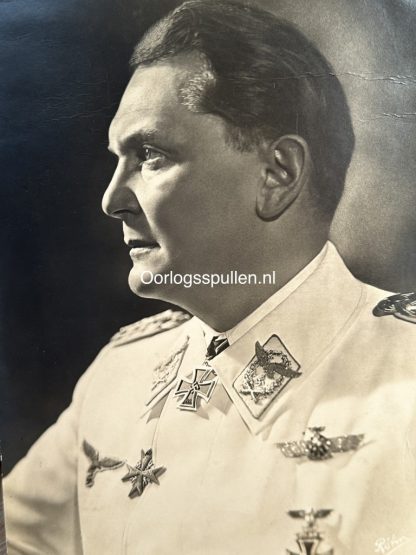 Black and white portrait photograph of Hermann Göring, a high-ranking Nazi official, wearing a white military uniform adorned with various medals and insignia. The photograph is taken from a side profile, showing his facial features in strong lighting. The watermark 'Oorlogsspullen.nl' is visible in the center of the image.