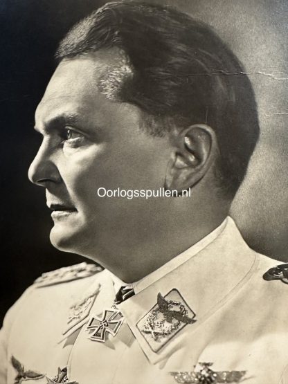 Black and white portrait photograph of Hermann Göring, a high-ranking Nazi official, wearing a white military uniform adorned with various medals and insignia. The photograph is taken from a side profile, showing his facial features in strong lighting. The watermark 'Oorlogsspullen.nl' is visible in the center of the image.