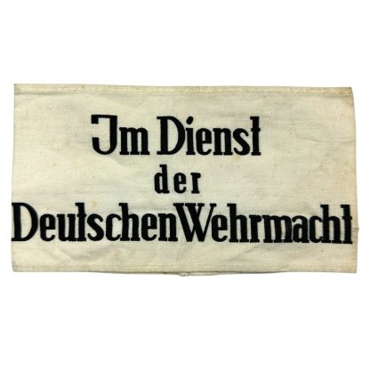 A historical WWII-era German armband made of white fabric with black printed text reading 'Im Dienst der Deutschen Wehrmacht,' meaning 'In the Service of the German Wehrmacht.' The fabric shows signs of aging with minor stains and creases.