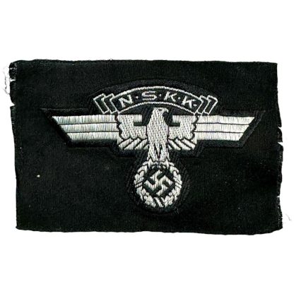 An unissued German NSKK (National Socialist Motor Corps) cap insignia patch from World War II. The black fabric patch features a silver-gray embroidered eagle with outstretched wings, clutching a swastika in its talons, with the letters 'N.S.K.K.' displayed above. The patch appears to be in mint condition, with no visible wear or signs of prior use.