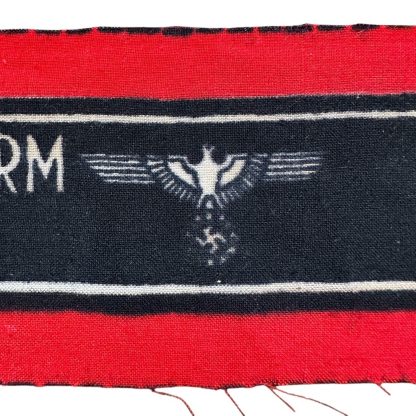 A WWII-era German Volkssturm armband, featuring a red and black design with white lettering reading 'DEUTSCHER VOLKSSTURM WEHRMACHT' and an eagle and swastika emblem. The fabric appears unissued, with frayed edges.