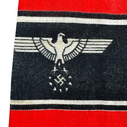 A WWII-era German Volkssturm armband featuring a red fabric background with a black central band, bordered by white stripes. The text 'DEUTSCHER VOLKSSTURM WEHRMACHT' is printed in white, alongside an eagle and swastika emblem. The fabric appears worn with frayed edges.