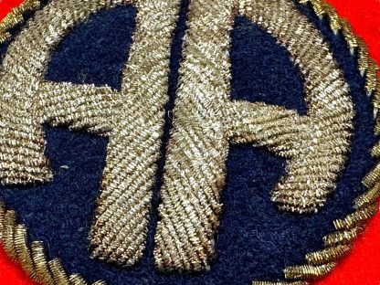 A World War II-era U.S. 82nd Airborne Division bullion patch, British-made. The patch consists of a curved black tab with 'AIRBORNE' embroidered in gold bullion thread and a square red patch featuring a gold bullion 'AA' insignia on a dark blue background, surrounded by gold braiding.