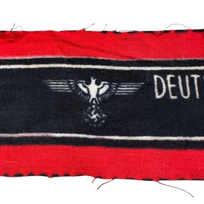 A WWII-era German Volkssturm armband, featuring a red and black design with white lettering reading 'DEUTSCHER VOLKSSTURM WEHRMACHT' and an eagle and swastika emblem. The fabric appears unissued, with frayed edges.