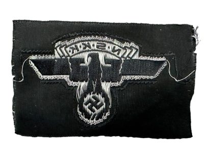 An unissued German NSKK (National Socialist Motor Corps) cap insignia patch from World War II. The black fabric patch features a silver-gray embroidered eagle with outstretched wings, clutching a swastika in its talons, with the letters 'N.S.K.K.' displayed above. The patch appears to be in mint condition, with no visible wear or signs of prior use.