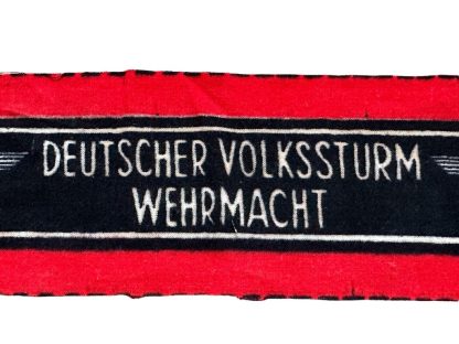 A WWII-era German Volkssturm armband, featuring a red and black design with white lettering reading 'DEUTSCHER VOLKSSTURM WEHRMACHT' and an eagle and swastika emblem. The fabric appears unissued, with frayed edges.