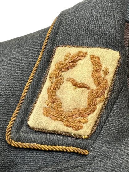 Close-up of a WWII German Luftwaffe General's tunic collar tab, featuring gold-embroidered oak leaves surrounding a Luftwaffe eagle on a beige background, bordered with gold braiding on a dark blue-gray wool base.