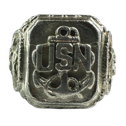 A vintage silver-tone United States Navy (USN) ring from World War II, featuring a raised emblem of an anchor with the letters 'USN' prominently displayed on the face. The ring has intricate engravings on the sides, showing detailed military-themed designs, and appears worn, indicating its historical significance.