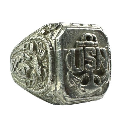 A vintage silver-tone United States Navy (USN) ring from World War II, featuring a raised emblem of an anchor with the letters 'USN' prominently displayed on the face. The ring has intricate engravings on the sides, showing detailed military-themed designs, and appears worn, indicating its historical significance.