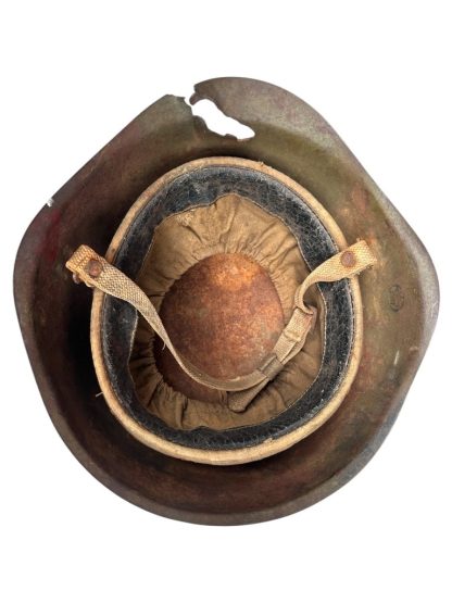 Interior view of a battle-damaged WWII Soviet SSh-39 steel helmet. The helmet’s liner is intact but aged, featuring a worn leather and cloth suspension system with frayed straps. The metal shell shows significant damage, including a large puncture and deformation along the rim. The interior metal surface is rusted, indicating extensive use and exposure to the elements.