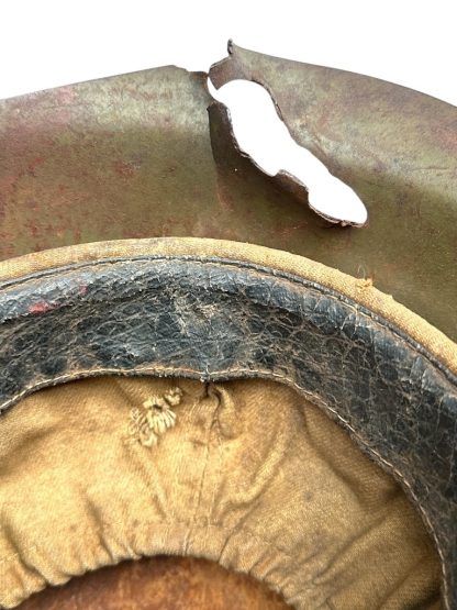 Close-up view of the interior of a battle-damaged WWII Soviet SSh-39 steel helmet. The helmet's liner, made of cloth and black leather, appears aged and worn, with visible stitching and fraying. The metal shell has a large, jagged hole along the rim, showing extensive war damage, possibly from shrapnel or a bullet impact. The surface has a greenish-brown patina with rust and scratches, indicating battlefield exposure.