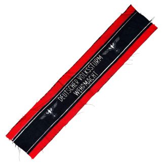 A WWII-era German Volkssturm armband, featuring a red and black design with white lettering reading 'DEUTSCHER VOLKSSTURM WEHRMACHT' and an eagle and swastika emblem. The fabric appears unissued, with frayed edges.