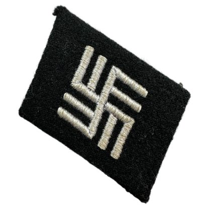 A historical black fabric collar tab with silver embroidered runic-style insignia, associated with Waffen-SS temporary concentration camp guards during World War II. The patch has a distinct geometric design and is set against a plain white background.