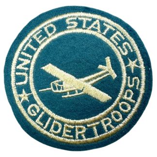 A World War II-era U.S. Glider Troops pocket patch. The patch is circular with a blue-green wool background and features embroidered gold lettering and design. 'UNITED STATES GLIDERTROOPS' is stitched around the outer edge, separated by two stars. The center showcases an embroidered glider in flight, symbolizing the airborne glider infantry. The patch was designed to be worn on the uniform pocket.