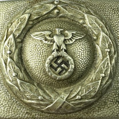 A silver-colored German DLV (Deutscher Luftsportverband) belt buckle featuring an embossed eagle with outstretched wings clutching a wreath enclosing a swastika, set against a pebbled-textured background with a decorative laurel wreath border."