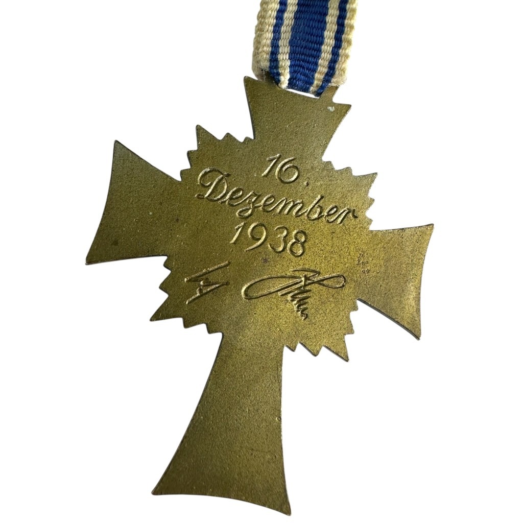 The reverse side of the German Mother's Cross in Bronze, engraved with the date "16 Dezember 1938" and a facsimile signature of Adolf Hitler. The bronze finish is visible, showing signs of age and wear.