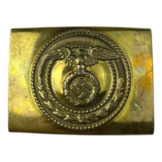 A brass-colored German SA belt buckle featuring an embossed eagle with outstretched wings clutching a wreath that encloses a swastika, surrounded by a decorative circular border.