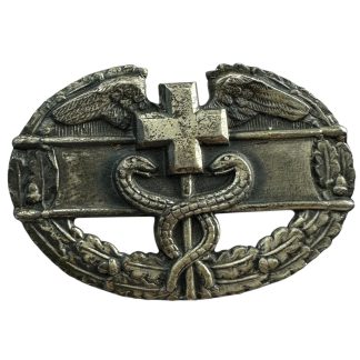 Original WWII U.S. Medical Combat Badge, featuring a central cross with a caduceus symbol of two intertwined snakes, flanked by wings and a laurel wreath. The badge is metallic with an aged patina, representing military medical personnel who served in combat conditions.