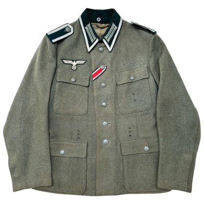 Original WWII German Wehrmacht M43 NCO field jacket in feldgrau (field gray) wool, featuring shoulder boards, collar tabs, an eagle-and-swastika breast eagle insignia, and a ribbon bar for the Iron Cross 2nd Class. The jacket has four front pockets with button closures and a five-button front closure.